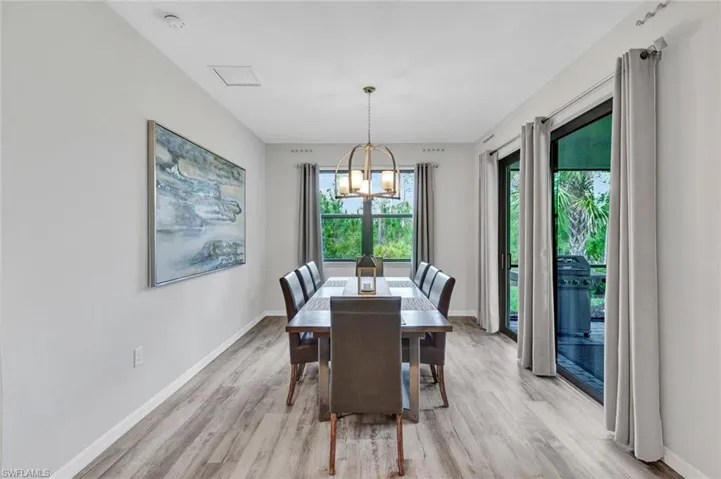 Inviting dining area featuring wood-finish flooring, a contemporary chandelier, a large window, and sliding glass doors providing access to an outdoor area