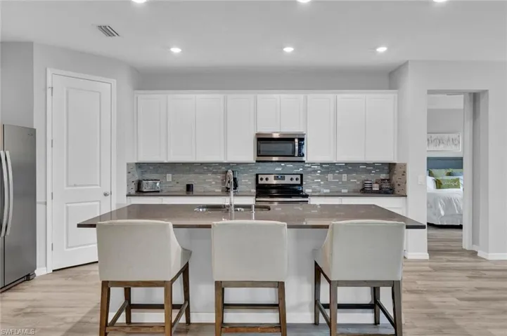 Kitchen featuring an island with seating, stainless steel appliances, white cabinetry, a decorative tile backsplash, and recessed lighting