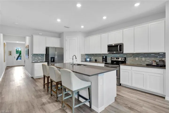 Open-concept kitchen featuring an island with counter seating, stainless steel appliances, white cabinetry, a mosaic tile backsplash, and wood-finish flooring