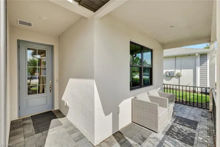 Covered front entry featuring a light blue paneled door with glass inserts, paver flooring, a black framed window, and a black metal railing