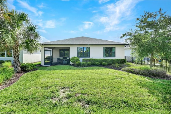 Expansive backyard featuring a manicured lawn, screened patio, and mature landscaping with a palm tree