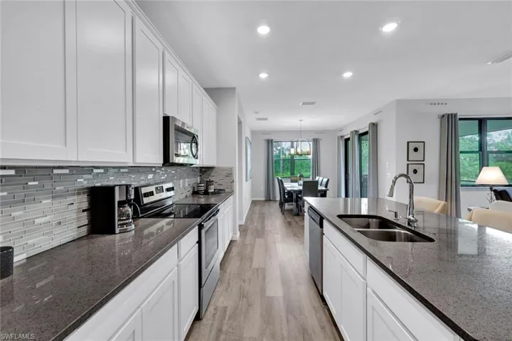 Spacious kitchen featuring white shaker-style cabinetry, dark stone countertops, and a full-height tile backsplash