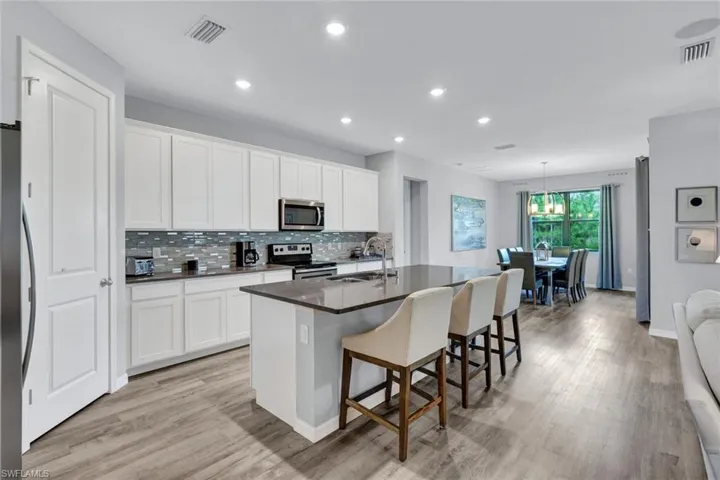 Kitchen featuring an expansive island with seating, extensive white cabinetry, a decorative tile backsplash, stainless steel appliances, and wood-finish flooring