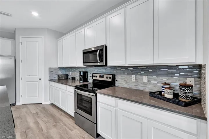 Kitchen featuring white shaker-style cabinetry, dark countertops, a mosaic tile backsplash, and stainless steel appliances including an oven range and microwave