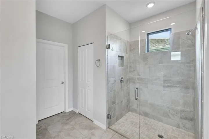 Spacious shower featuring clear glass enclosure, large format tile walls, mosaic tile floor, and an integrated shower niche