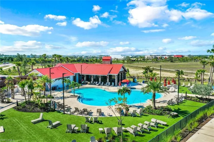 Resort-style pool area featuring a large freeform swimming pool, extensive sun deck with lounge chairs, and a contemporary clubhouse with a red metal roof