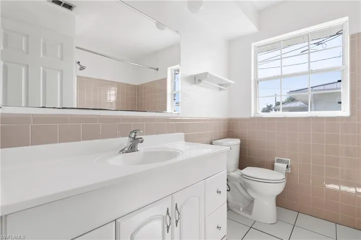 Bathroom with tile walls, tile patterned flooring, a wealth of natural light, and toilet