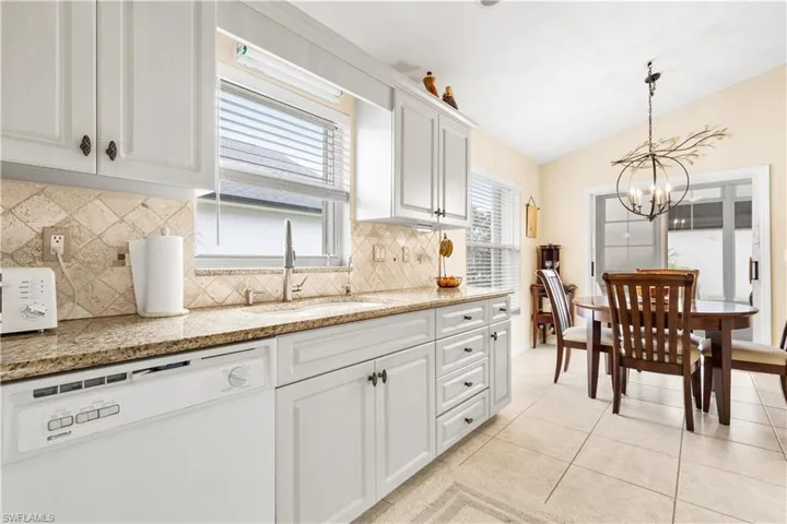 Kitchen with white dishwasher, sink, white cabinets, hanging light fixtures, and light tile patterned flooring