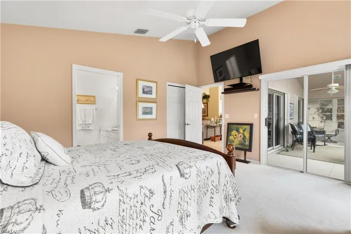 Bedroom with ensuite bathroom, ceiling fan, light carpet, and vaulted ceiling
