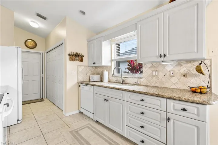 Kitchen featuring white appliances, sink, light stone countertops, light tile patterned floors, and white cabinetry