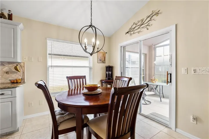 Tiled dining room with a healthy amount of sunlight, vaulted ceiling, and an inviting chandelier
