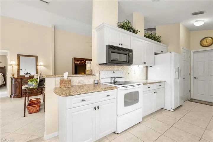 Kitchen with white cabinetry, light stone counters, white appliances, and light tile patterned floors