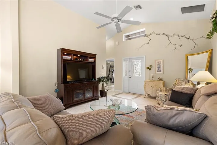 Living room with ceiling fan, light tile patterned flooring, and high vaulted ceiling