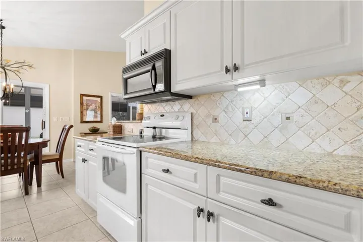 Kitchen featuring light tile patterned floors, tasteful backsplash, light stone counters, electric stove, and white cabinets