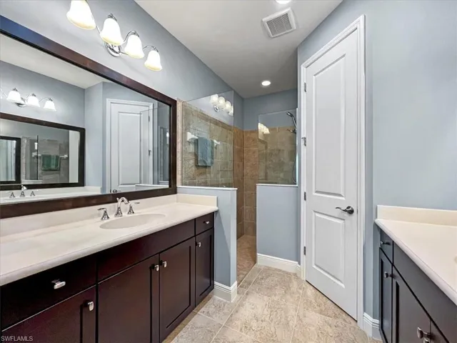 Bathroom with vanity, tile patterned flooring, framed mirror and a tile shower