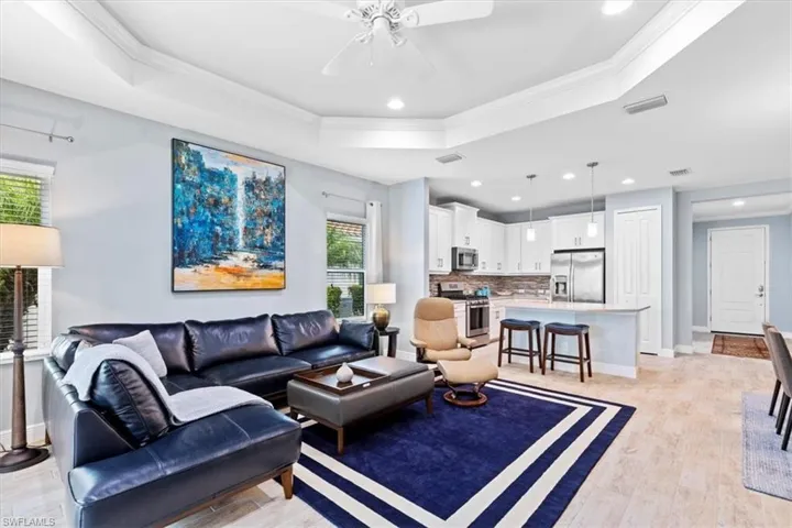 Living room with light hardwood / wood-style floors, a raised ceiling, crown molding, and ceiling fan