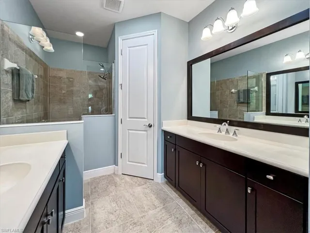 Bathroom with tile patterned flooring, double sink vanity, framed mirror and tiled shower