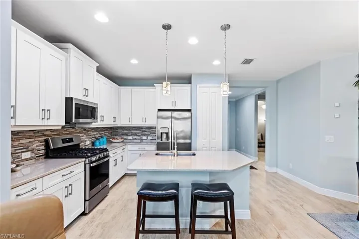 Kitchen with tasteful backsplash, stainless steel appliances, a center island with sink, decorative light fixtures, and light wood-type flooring