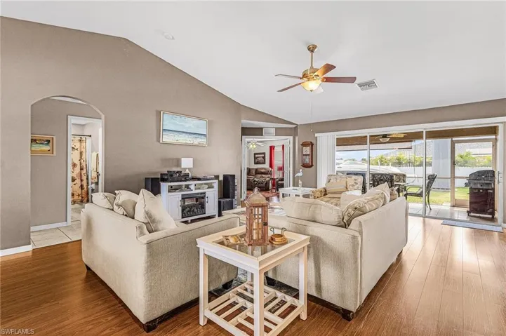 Living room featuring a ceiling fan, arched walkways, wood finished floors, and high vaulted ceiling