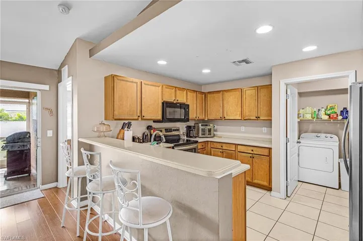 Kitchen featuring washer / clothes dryer, stainless steel appliances, light countertops, a breakfast bar, and a peninsula
