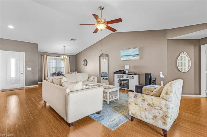 Living area featuring a ceiling fan, wood finished floors, vaulted ceiling, and a chandelier