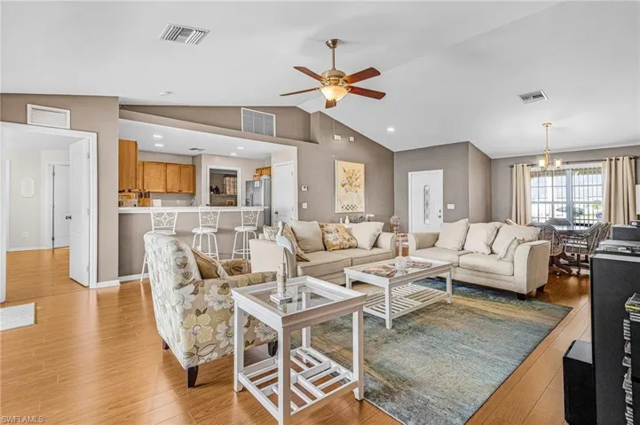 Living area with ceiling fan, a chandelier, light wood-style floors, and lofted ceiling