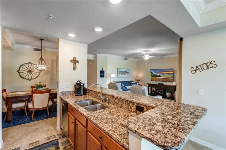 Kitchen featuring a sink, crown molding, brown cabinets, open floor plan, and light stone countertops