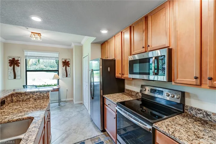 Kitchen featuring stainless steel appliances, crown molding, baseboards, light stone counters, and a sink