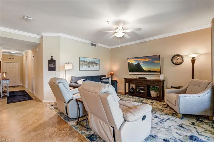 Living room with a ceiling fan, crown molding, tile patterned flooring, and baseboards