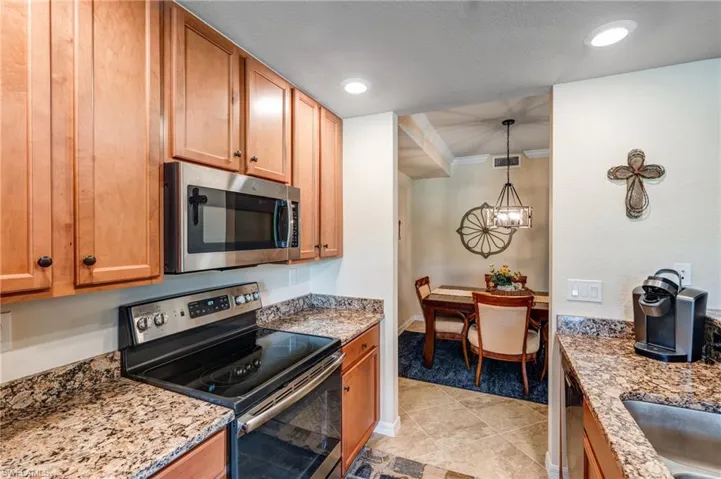 Kitchen featuring appliances with stainless steel finishes, a chandelier, light stone counters, crown molding, and light colored carpet