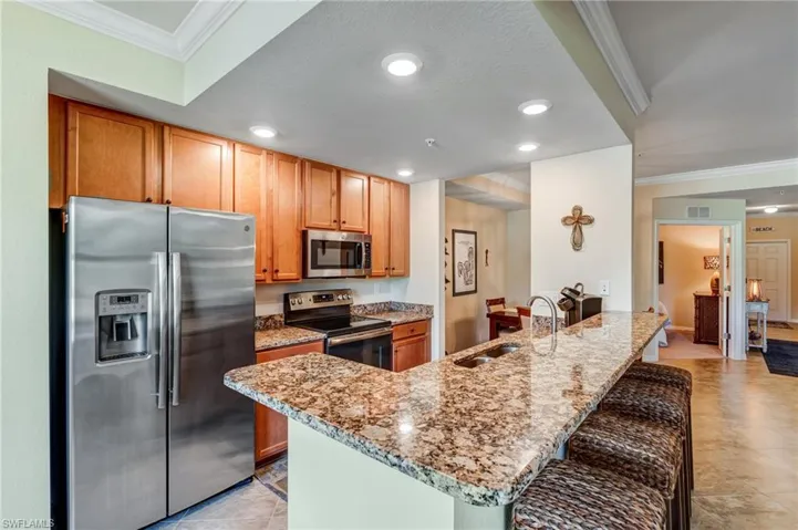 Kitchen with appliances with stainless steel finishes, a sink, a kitchen breakfast bar, light stone counters, and crown molding