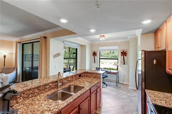 Kitchen featuring a sink, freestanding refrigerator, baseboards, ornamental molding, and light stone countertops