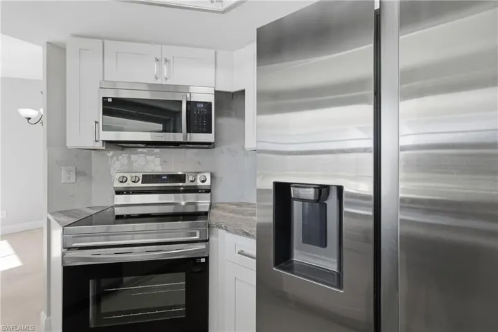 Kitchen featuring stainless steel appliances, white cabinetry, light stone countertops, and tasteful backsplash