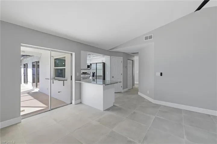 Kitchen featuring a peninsula, appliances with stainless steel finishes, lofted ceiling, white cabinetry, and dark stone countertops