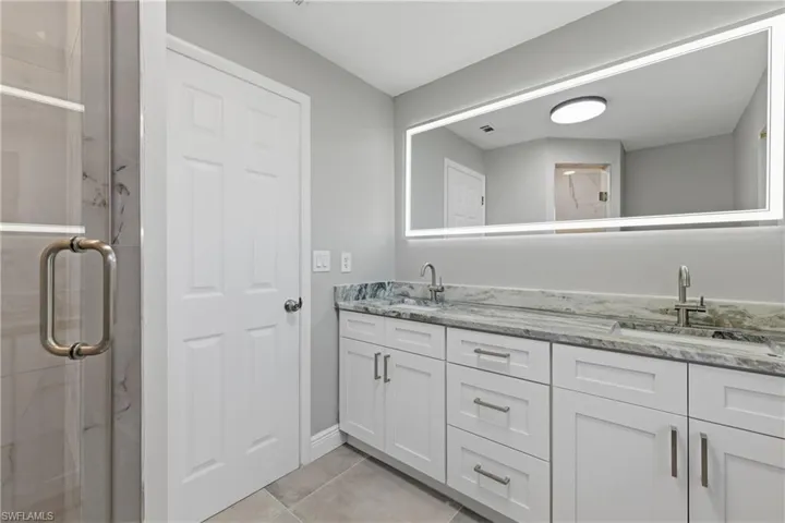 Full bath with double vanity, a marble finish shower, and light tile patterned floors