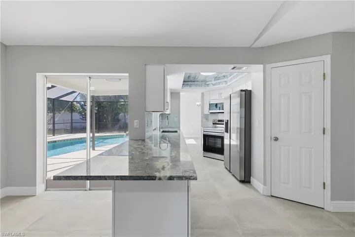 Kitchen with white cabinets, dark stone counters, stainless steel appliances, a sunroom, and a peninsula