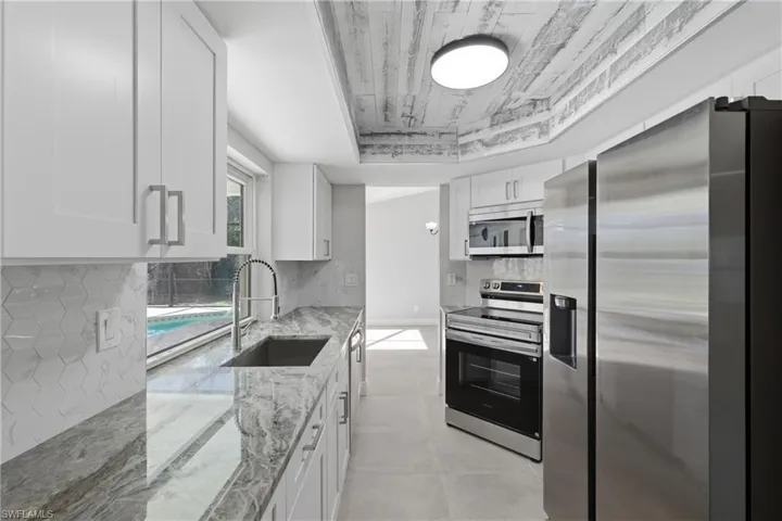 Kitchen featuring stainless steel appliances, light stone counters, white cabinets, a raised ceiling, and wood ceiling