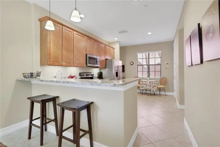 Kitchen featuring a breakfast bar, a peninsula, light tile patterned floors, light stone counters, and recessed lighting