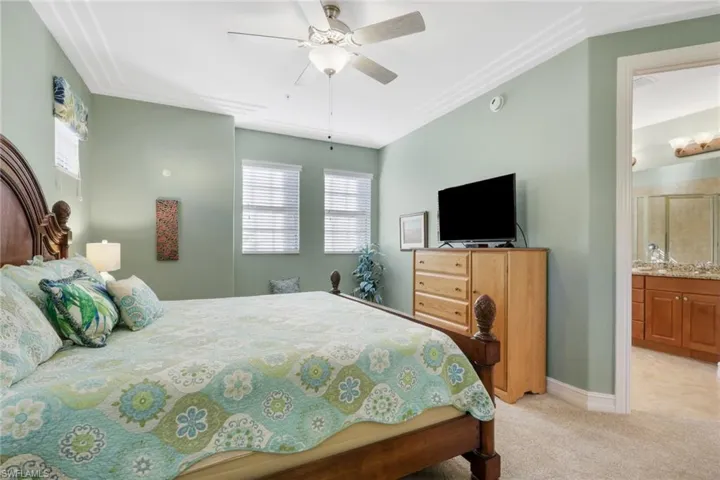 Bedroom featuring ceiling fan, light carpet, and ensuite bathroom