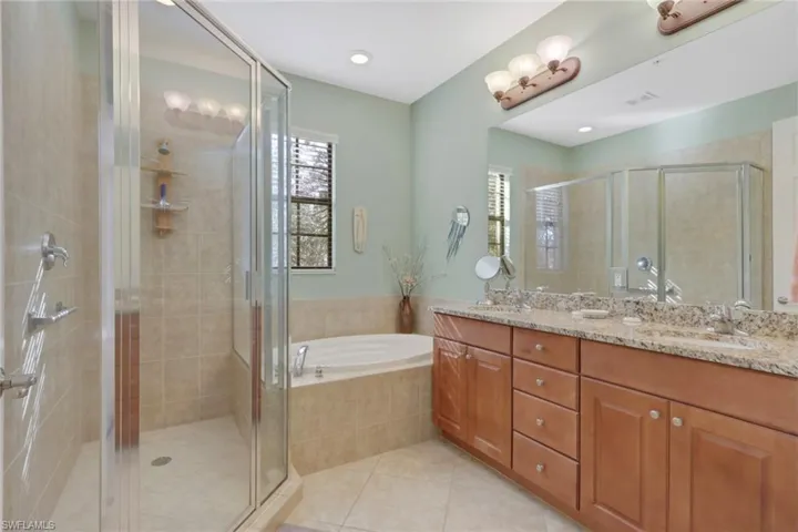 Bathroom featuring double vanity, a garden tub, a stall shower, and light tile patterned flooring