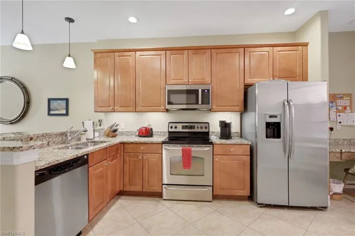Kitchen with appliances with stainless steel finishes, light stone countertops, decorative light fixtures, a peninsula, and brown cabinetry