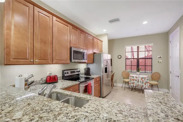 Kitchen with stainless steel appliances, light stone countertops, light tile patterned flooring, brown cabinets, and recessed lighting