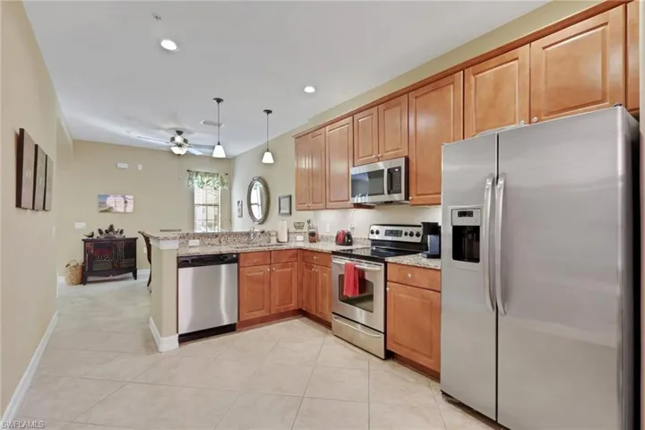 Kitchen featuring appliances with stainless steel finishes, light stone counters, decorative light fixtures, light tile patterned floors, and brown cabinets