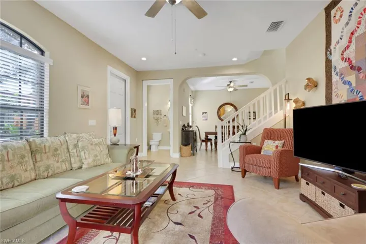 Living area featuring stairs, tile patterned flooring, a ceiling fan, and arched walkways