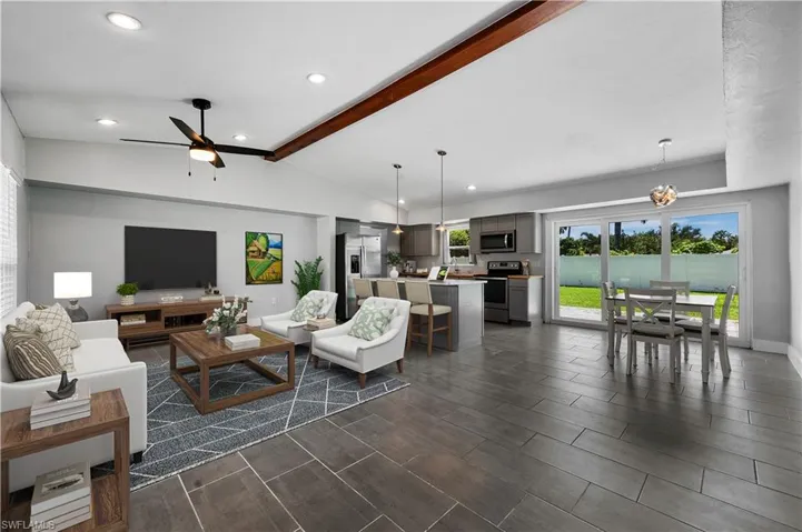 Living room with ceiling fan with notable chandelier and vaulted ceiling with beams