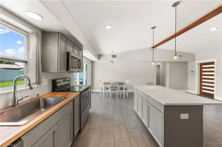 Kitchen with a center island, gray cabinets, appliances with stainless steel finishes, vaulted ceiling, and sink