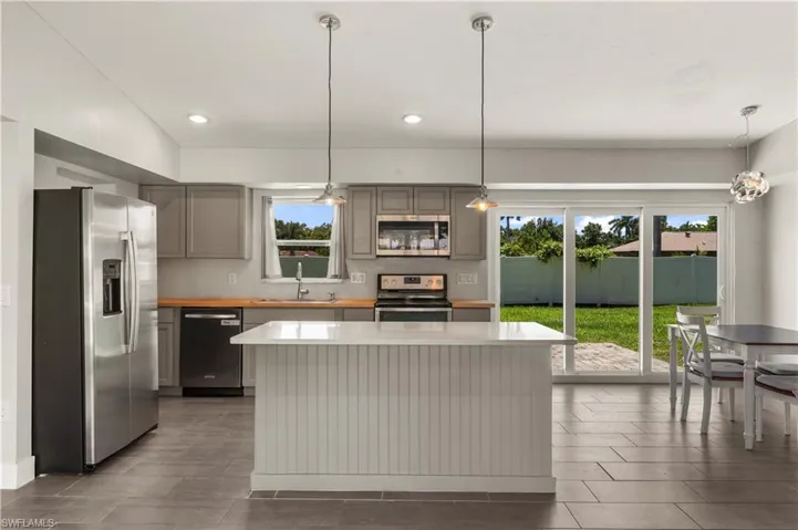 Kitchen with appliances with stainless steel finishes, sink, pendant lighting, gray cabinets, and a kitchen island