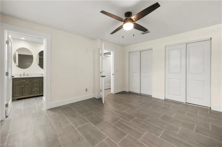Unfurnished bedroom with two closets, ensuite bath, ceiling fan, and sink