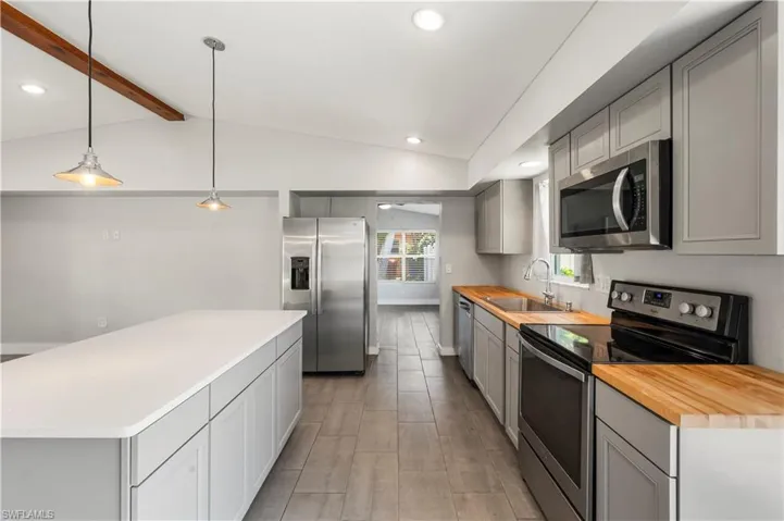Kitchen featuring gray cabinets, sink, lofted ceiling with beams, a kitchen island, and appliances with stainless steel finishes