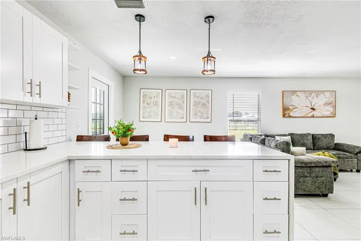 Kitchen featuring white shaker-style cabinetry, a stone-surface island, subway tile backsplash, and dual hanging pendant lights, complemented by large-format tile flooring